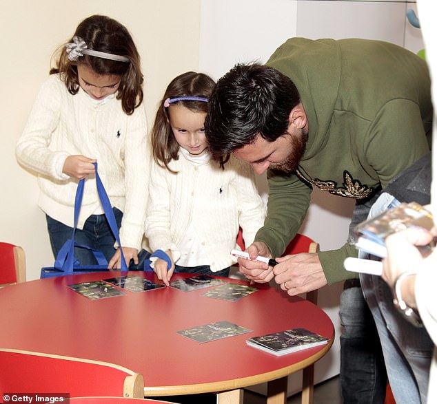 Striker Messi, wearing a green hoodie, held a pen as he signed multiple photos for children